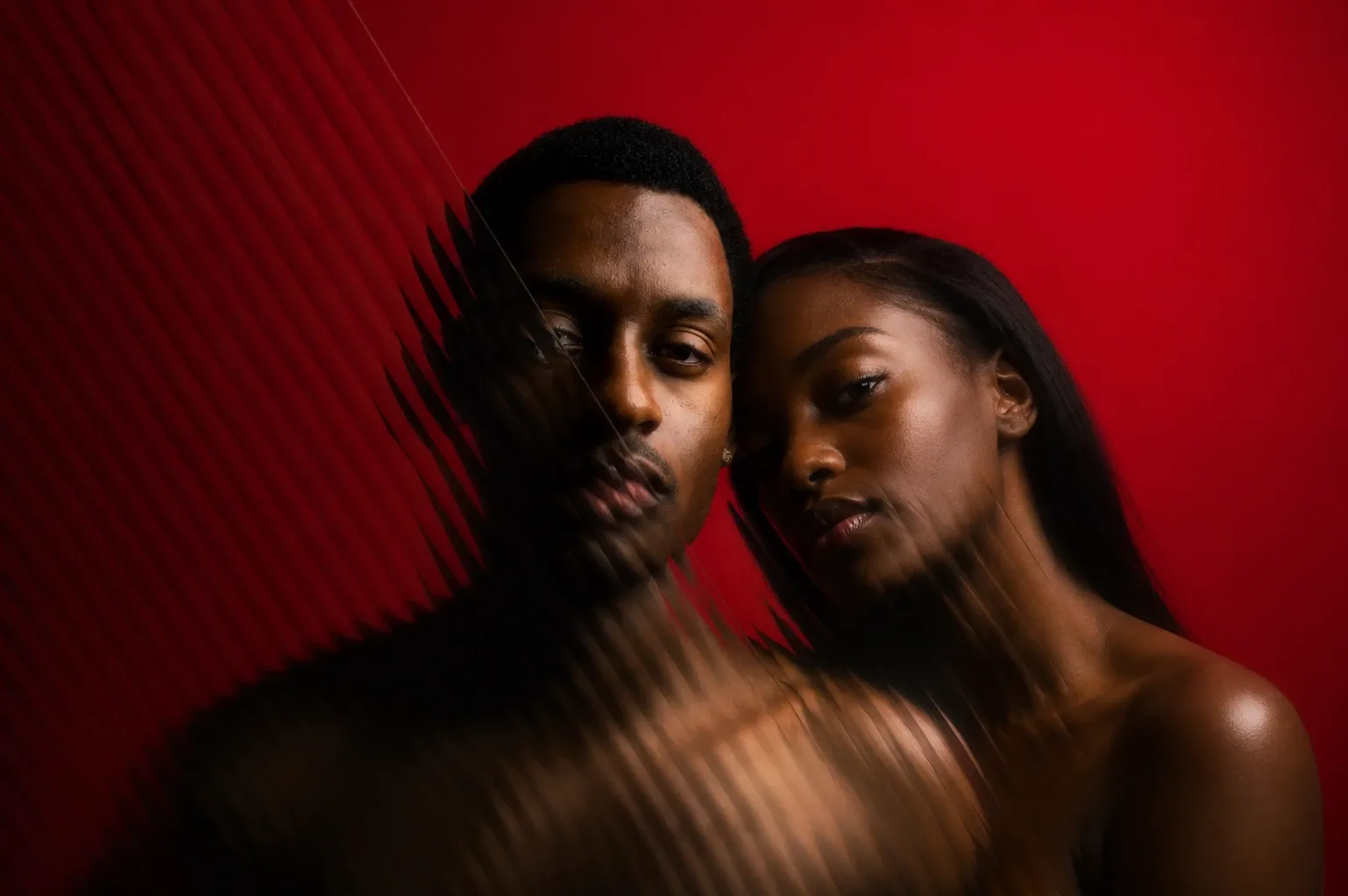 A couple pressed close together against a red wall, seen through ribbed glass