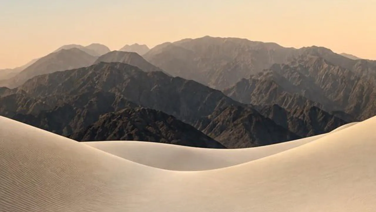 Desktop wallpaper: pale sand dunes in front of dark mountains at sunset